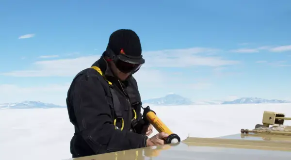 Hombre con equipo de seguridad usa pistola aplicadora de **productos químicos** para sellar una superficie en un paisaje nevado.
