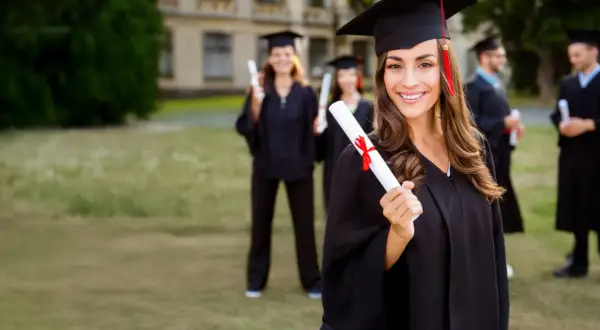 Absolventin mit Urkunde, bereit für MBA mit Fachwirt. Mehrere Studenten in Roben im Hintergrund.