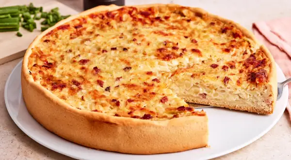 Ein goldbrauner Zwiebelkuchen mit Speck, bereit zum Servieren. Ein Stück fehlt, was Lust auf mehr macht. Perfekt für ein Zwiebelkuchen Rezept.