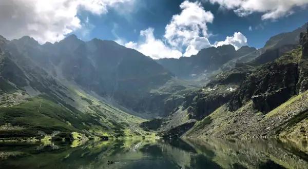 Malowniczy widok na Czarny Staw Gąsienicowy. Trasa wije się po zboczu, a w tafli jeziora odbijają się góry i chmury.