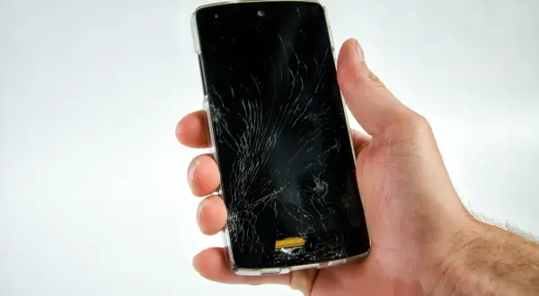 Dłoń trzyma pęknięty telefon, który nie chce się włączyć.