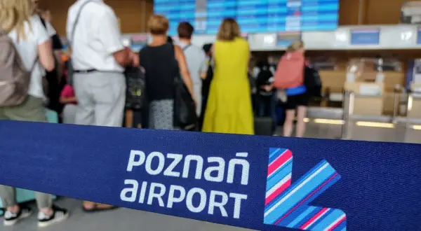 Niebieska taśma z napisem "POZNAŃ AIRPORT" i logo lotniska na tle ludzi i tablicy odlotów.