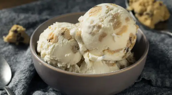 Schüssel mit cremigem Eis, durchzogen von Stückchen aus süßem Keksteig und Schokoladenstückchen. Ein Löffel liegt daneben.