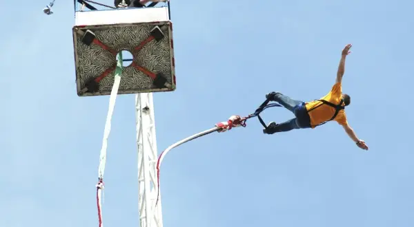 Człowiek w żółtej koszulce skacze na bungee. Zastanawiasz się, ile kosztuje skok na bungee? To niezapomniane przeżycie!