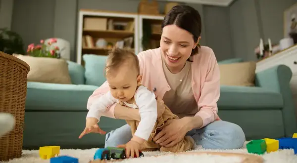 Mama z dzieckiem bawią się pociągiem na dywanie. Każde dziecko to skarb, a inwestycja 12 tys na dziecko to piękny początek.