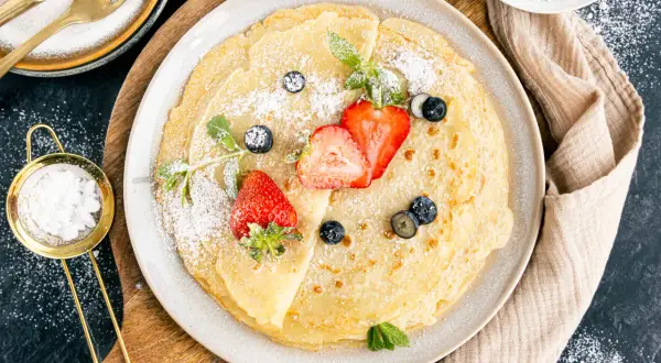 Dünne Pfannkuchen mit Hafermilch, bestäubt mit Puderzucker und garniert mit frischen Erdbeeren und Blaubeeren.