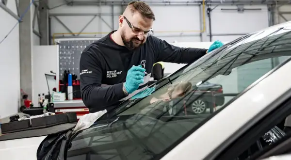 Mechanik w okularach ochronnych i rękawiczkach naprawia szybę samochodową.