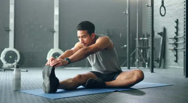 Mann dehnt sich im Fitnessstudio, um den Muskelaufbau zu unterstützen.