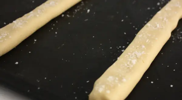 Två degstänger med flingsalt på en svart plåt, redo att bli ljuvliga kolakakor.