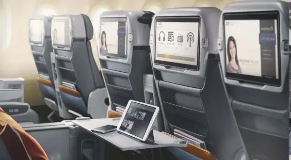 Komfortowe fotele w klasie lot premium economy. Ekrany rozrywki pokładowej, tablet i telefon na stoliku.