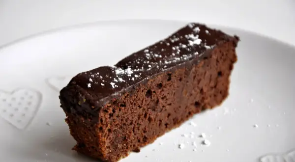 Wilgotny brownie z fasoli, polany czekoladą i posypany cukrem pudrem, na białym talerzu z serduszkami.