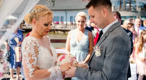 Para młoda podczas ceremonii ślubnej. Panna młoda w koronkowej sukni, pan młody w garniturze. Pytanie o to, odpis aktu małżeństwa ile ważny, nie ma związku z tą sceną.
