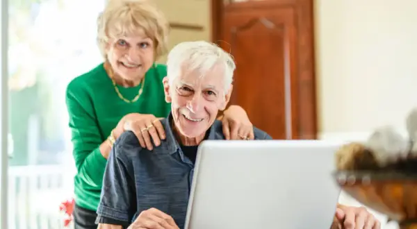 Couple souriant devant un ordinateur, discutant de l'obligation alimentaire en EHPAD et des impôts.