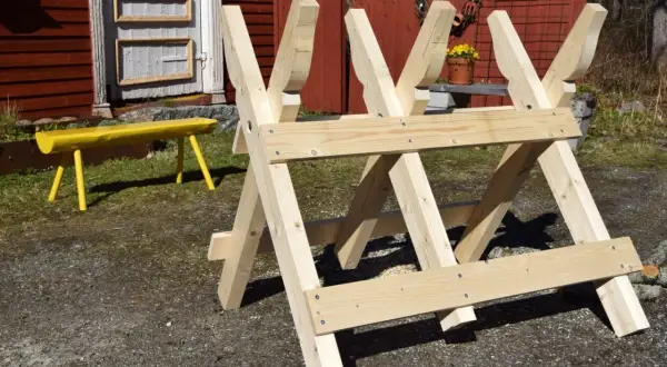 En nybyggd sågbock ritning i trä, redo för vedhuggning. En gul bänk syns i bakgrunden.