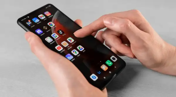 Dłoń dotyka ekranu smartfona z ikonami aplikacji. Dowiedz się, jak usunąć subskrypcję z telefonu, przeglądając ustawienia lub aplikacje.