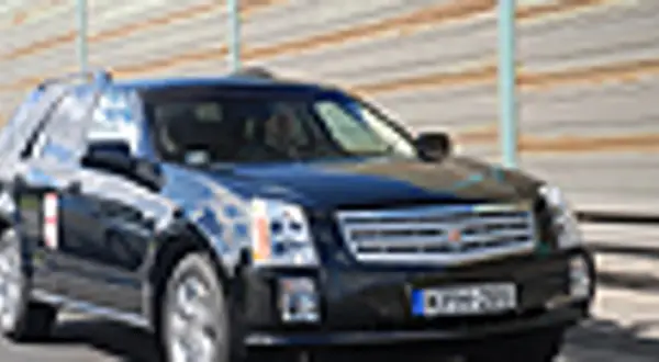 Czarny Cadillac SRX z przyciemnianymi szybami i chromowanymi detalami jedzie po drodze.