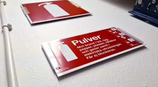 Röd skylt för pulverbrandsläckare, klassad brandklass A1. Informerar om att den släcker bränder i trä, tyg, papper, vätskor och gaser.