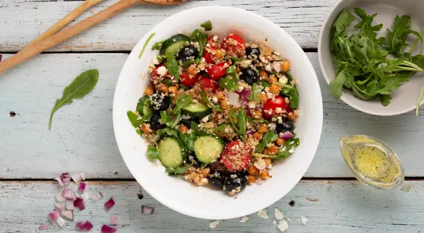 Insalata di quinoa colorata con ceci, pomodorini, olive, cetrioli e rucola. Un piatto fresco e salutare.