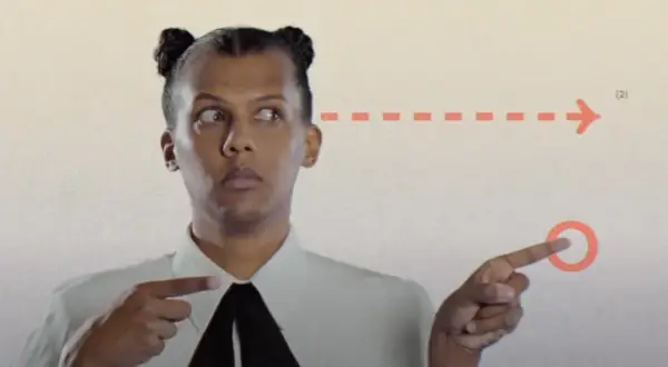 Stromae w Polsce, z charakterystycznymi kucykami, wskazuje na strzałkę.