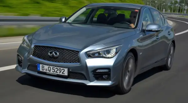 Srebrny infiniti samochód pędzi po autostradzie, kierowca w okularach przeciwsłonecznych cieszy się jazdą.
