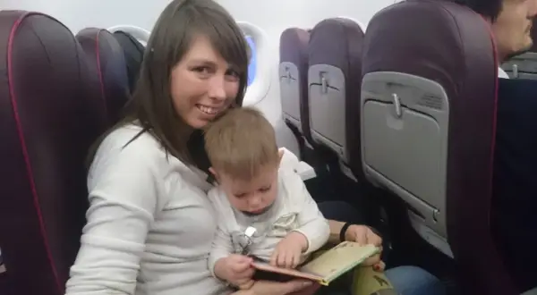 Mama z dzieckiem w samolocie Wizzair. Dziecko przegląda książeczkę, siedząc na kolanach mamy.
