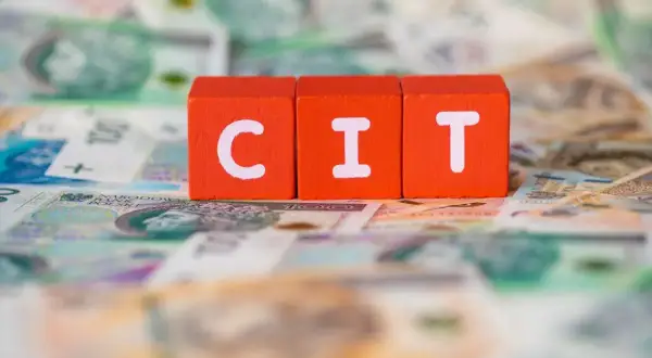 Trzy pomarańczowe klocki z literami "C", "I", "T" leżą na tle polskich banknotów. Podatek CIT to ważna część finansów.