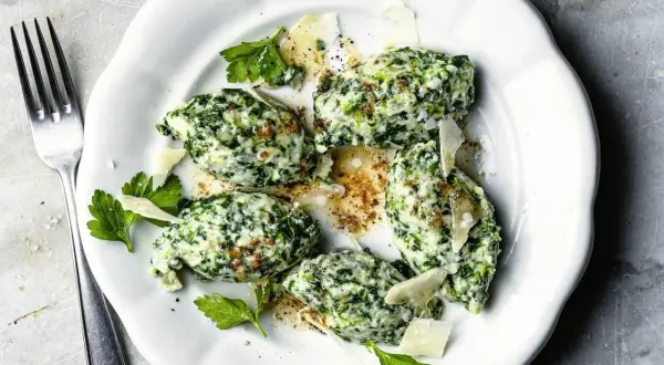 Malfatti Rezept: Grüne Klößchen aus Spinat und Ricotta, garniert mit Parmesan und Petersilie, auf einem weißen Teller.