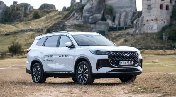 Biały Chery Tiggo 8 Plug-in Hybrid z zasięgiem do 1100 km, zaparkowany na tle ruin zamku. Sprawdź jego cenę!