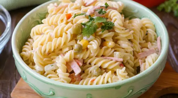 Ein cremiger Nudelsalat mit Erbsen, Mais und Schinkenwürfeln, der an einen herzhaften Fleischsalat erinnert. Garniert mit Petersilie.