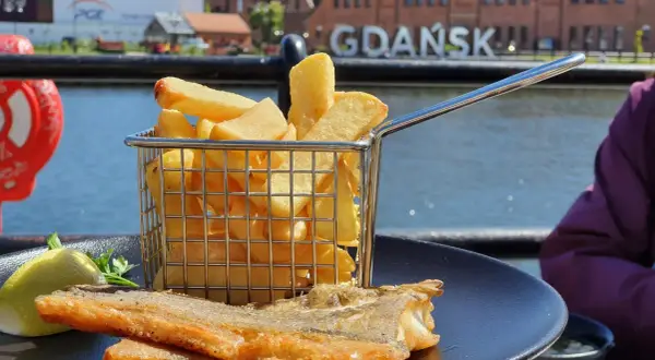 Ryba z frytkami na talerzu, w tle napis GDAŃSK. Idealne miejsce, gdzie zjeść w Gdańsku.