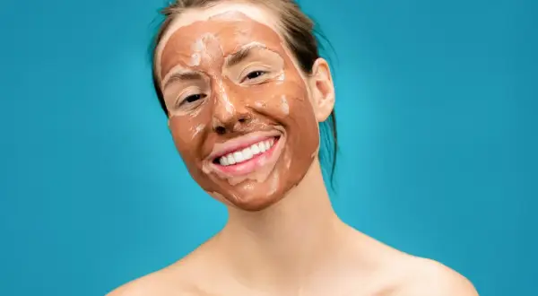 Ragazza sorridente con una maschera all'argilla sul viso, che promette un viso lucido e radioso.
