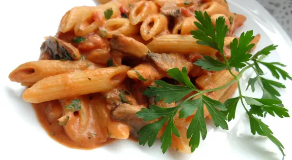 Penne z kremowym sosem pomidorowym i pieczarkami, udekorowane natką pietruszki. Pyszny makaron z pieczarkami.