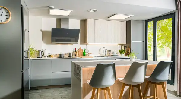 Moderna cocina con isla central, gabinetes grises y de madera, campana extractora negra y tres taburetes.