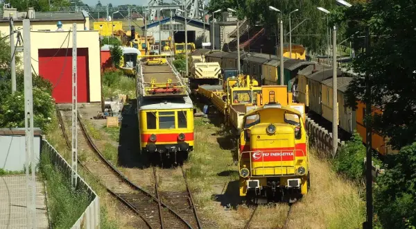 Dwie żółte lokomotywy, jedna z napisem "PKP Energetyka", stoją na torach w słoneczny dzień.