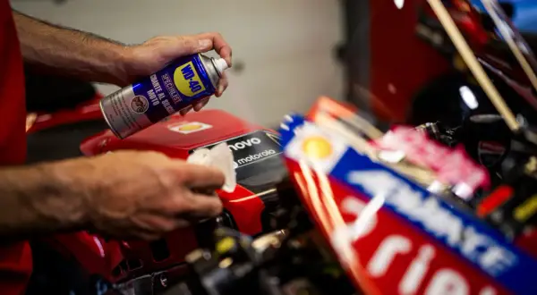 Mani che usano WD-40 per lucidare la plastica di una moto da corsa rossa, per un look brillante.