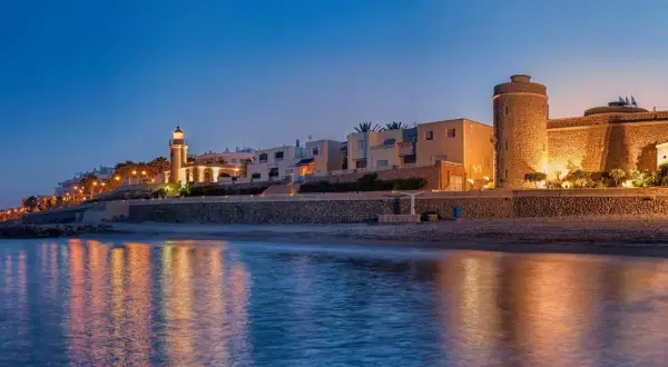Atardecer en Roquetas de Mar. Faro y castillo iluminados, reflejos en el mar. ¡Ideas de qué hacer en Roquetas de Mar!