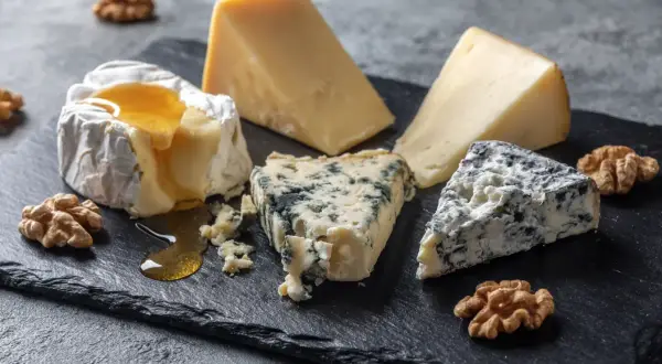 En ostbricka med brie, blåmögelost och en bit ost som påminner om ost comte, garnerad med valnötter och honung.