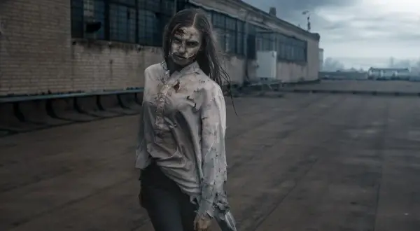 Przerażająca postać, jak z książek o zombie, stoi na dachu.