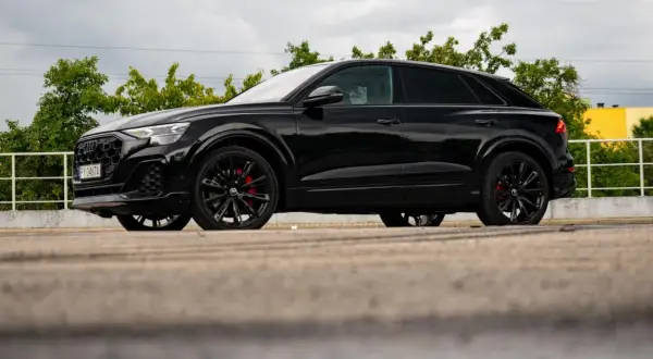 Czarny Audi Q9 z czerwonymi zaciskami hamulcowymi, odbijający się w kałuży. Sprawdź audi q9 cena!