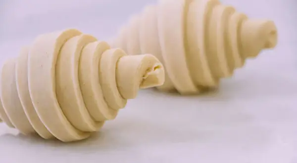 Dos croissants de mantequilla crudos, con sus capas visibles, listos para hornearse y deleitar.