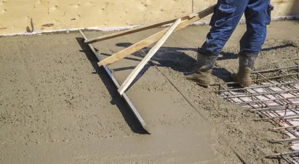 Pracownik wykonuje szlifowanie betonu za pomocą łaty, wyrównując świeżą nawierzchnię.