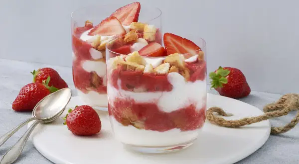 Zwei Gläser mit einem sommerlichen Dessert aus Erdbeeren und Sahne, garniert mit frischen Erdbeerscheiben und Keksstückchen. Ein schnell und einfach zubereitetes Genusserlebnis.