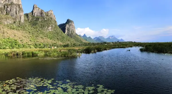 Khao Sam Roi Yot National Park: Majestätische Berge ragen über einen ruhigen Fluss mit Seerosen und Schilf auf.