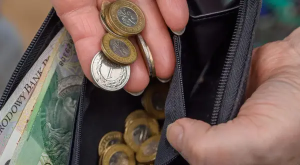 Dłoń z monetami i banknotami w portfelu. Zastanawiasz się, ile wynosi renta wojskowa?