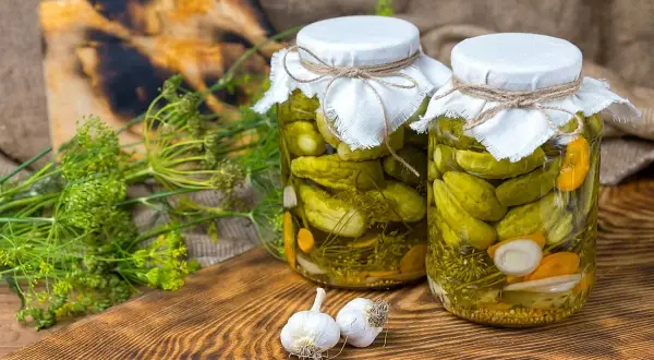 Słoiki z ogórkami korniszony, przygotowane według przepisu babci. Obok świeży koperek i czosnek.