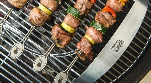 Spiedo di carne mista succulenta e verdure grigliate su una griglia Weber.