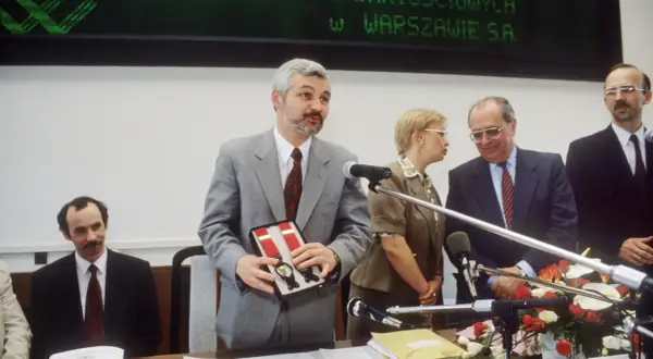 Uroczystość otwarcia, gdzie powstała pierwsza polska giełda. Mężczyzna w szarym garniturze prezentuje pudełko z szelkami.