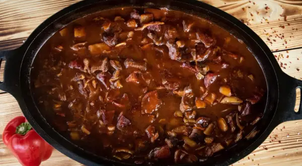 Herzhaftes Gulasch im Dutch Oven, ein Klassiker der Dutch Oven Rezepte. Daneben liegt eine rote Paprika.