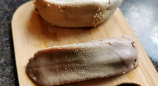 Dwa ugotowane ozory wieprzowe na desce, gotowe do obrania. To pierwszy krok, jak obrać ozory wieprzowe.