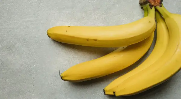 Trzy żółte banany leżą na szarym tle. Jeden banan kcal to zdrowa przekąska.